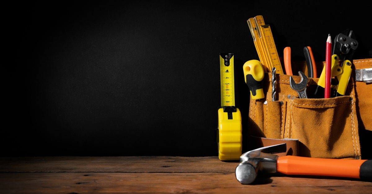 A pouch filled with basic home repair tools sitting on a wooden table against a pitch black background.
