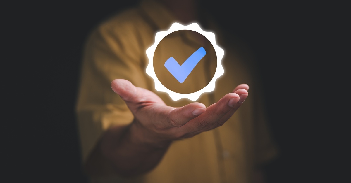 A digital warranty checkmark floating above the hand of a person in a yellow shirt, who is obscured by a black background.