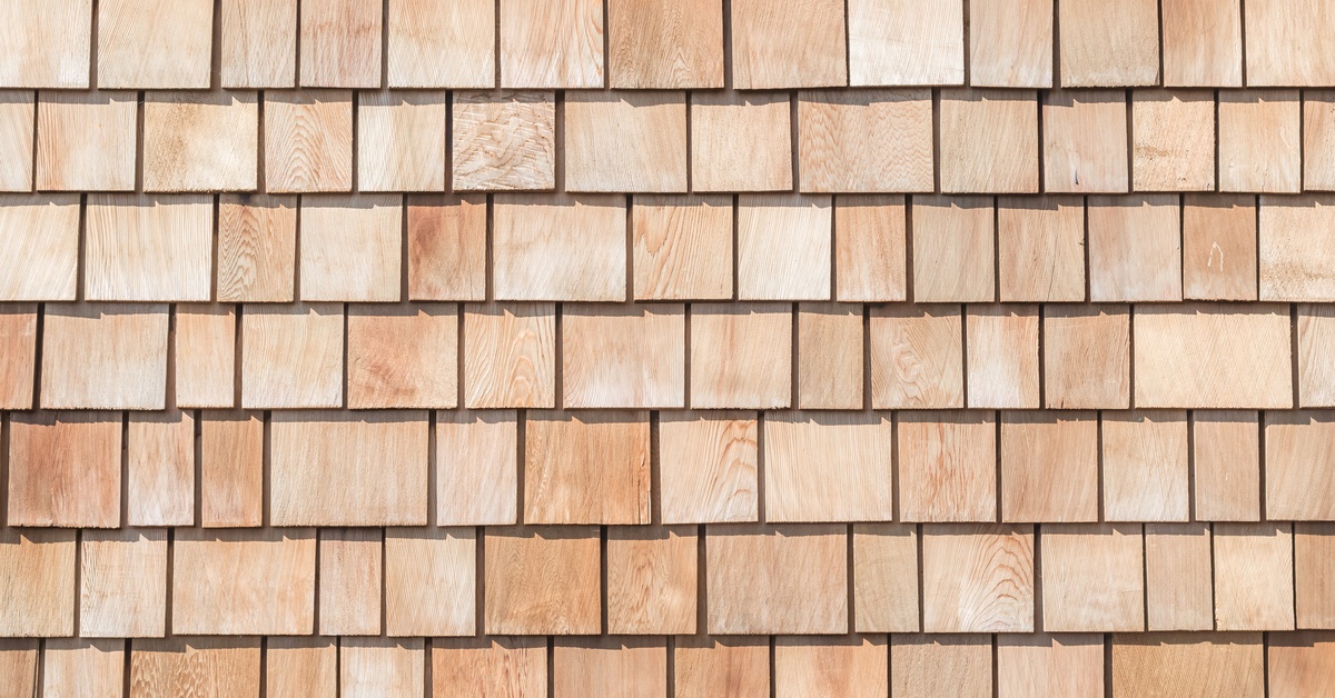 Beautiful Cabin Siding Ideas To Elevate Your Exterior A close-up of newly installed cedar shake siding. The sun shines from above, casting shadows below each shake.