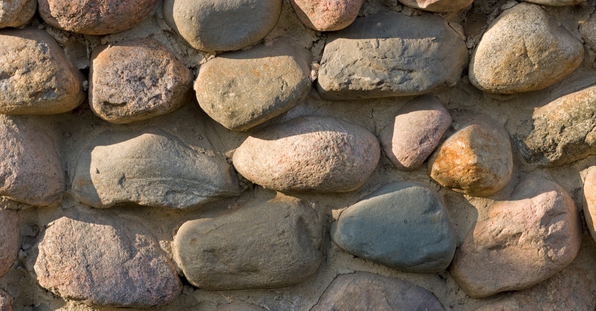 A close-up of rounded river stones set in mortar, showing a textured stone foundation wall in mixed earth tones.